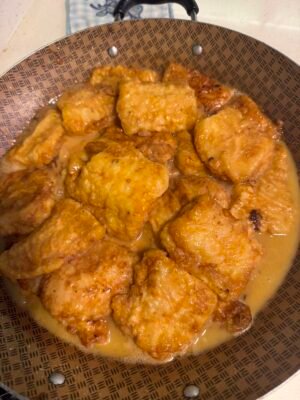 cooked fish or chicken pieces in fry pan with white wine and lemon juice sauce